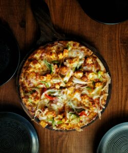 Mouthwatering close-up of a spicy paneer tikka pizza on a wooden table.