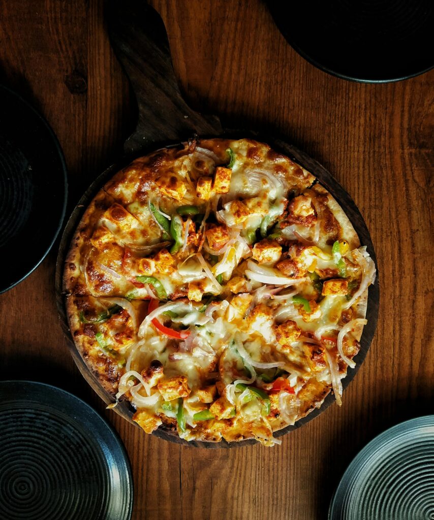 Mouthwatering close-up of a spicy paneer tikka pizza on a wooden table.