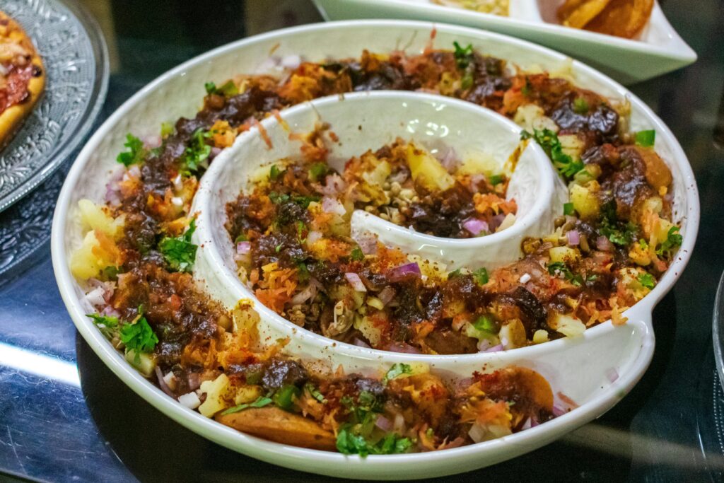 A vibrant and colorful spiral platter of Indian Aloo Chaat garnished with herbs.
