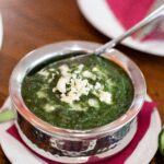 Top-down view of creamy palak paneer served in a stainless steel bowl, garnished with crumbled cheese.