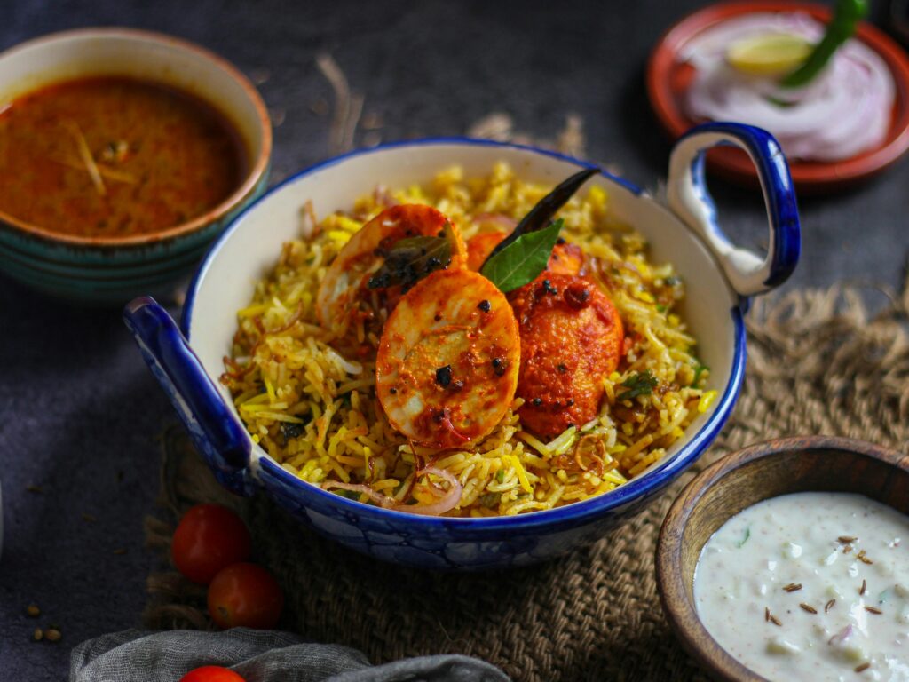 Close-up of spiced egg biryani with yogurt and curry side dishes, New Delhi.